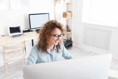 Happy student girl wearing glasses surfing high-speed internet on laptop pc. Hard-working student being busy with studyingの写真素材