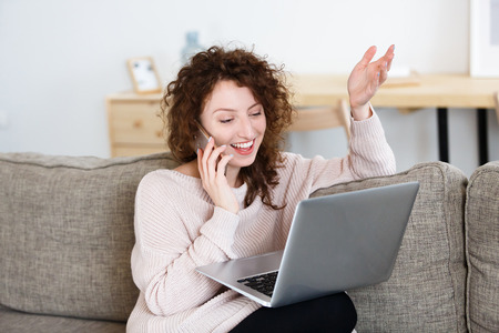 Charming glad caucasian female freelancer has phone conversation, surfing high-speed internet on laptop pc. People, technology, lifestyleの写真素材