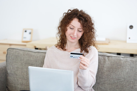 Satisfied redhead female with glad expression surfing high-speed internet on laptop pc, using credit card to pay for online purchase,paying bills onlineの写真素材