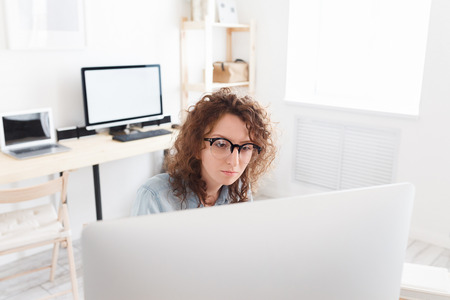 Indoor shot of serious concentrated business lady reads information on laptop computer, surfes internet in modern officeの写真素材