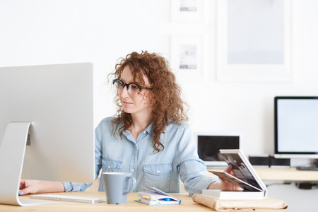 Young female journalist reads information on laptop computer, surfes internet, has pleasant smile. Attractive female freelancer works remotely at homeの写真素材