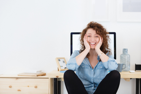 Pleased male freelancer sitting at desk in front of computer and demonstrates positive emotions or feelings, happy with completed work.の写真素材