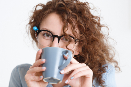Close up portrait of young caucasian female employee with curly red hair drinking her morning coffee.の写真素材