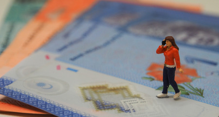 Miniature figure of woman talking on the phone walking on the Malaysian banknotesの写真素材