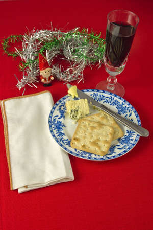 Two crackers and Stilton cheese on blue and white plate , with knife and butter. White napkin against red table cloth, with decorations.Glass of red wine.の写真素材