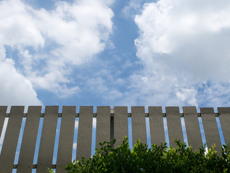 Brown fence with green leaves and blue sky background.の写真素材