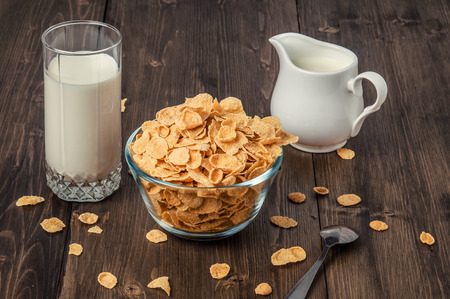 corn flakes with milk jug and glass on wooden table