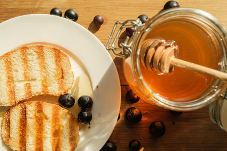 Slices of grilled toast accompanied by fresh blueberries and a jar of honey are arranged on a wooden...