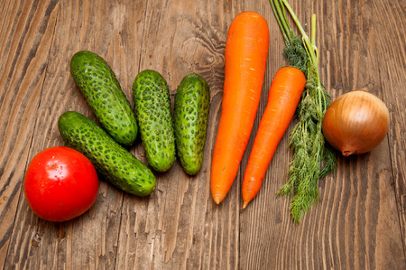 Tomato, cucumbers, carrots, herbs and onion on the wood tableの写真素材