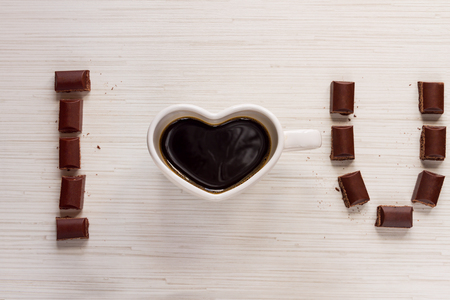 Cup with coffee shaped heart "i love you" and valentine's chocolate on wood backgroundの写真素材