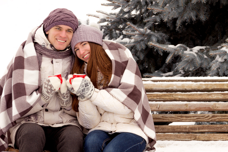 Happy couple in love in white outerwear siting and drink coffee in park in winterの写真素材