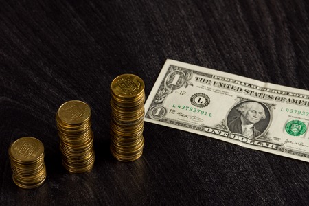 Economic crisis concept. Gold ukrainian stacks of coins and american one dollar on wooden backgroundの写真素材