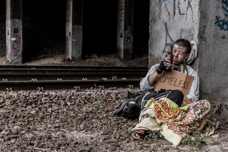 Homeless young woman drinking beer sitting near the rail trackの写真素材