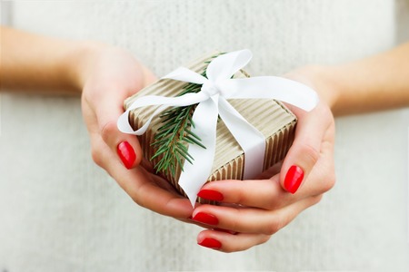 Girl holding decorated gift with white ribbon and branch of christmas treeの写真素材