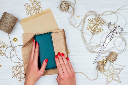 Gril wrapping up emerald-green notebook with colorful paper and decorationg with string and golden...