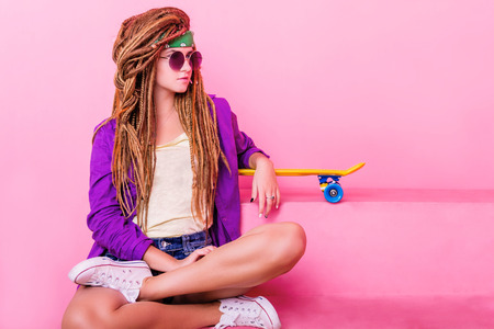 Pretty girl with dreadlocks and green do-rag sitting near the yellow skateboardの写真素材