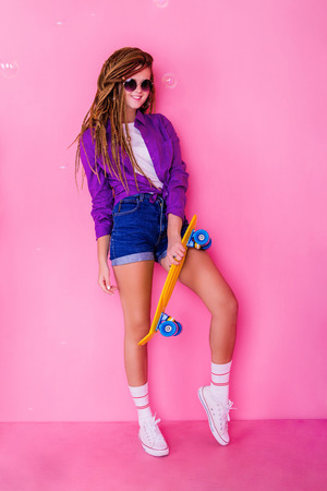 Pretty girl with dreadlocks and sunglasses holding yellow skateboard and smilingの写真素材