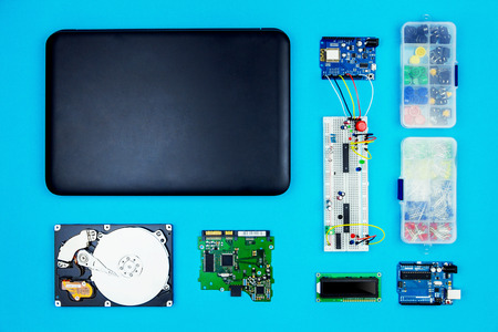 Top view of desktop of  hardware engineer on blue background. Black laptop with connectors, microcontroller, hdd and hardware equipmentの写真素材