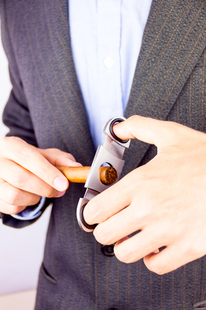 Elegant man wearing suit and blue shirt cutting cigar indoorの写真素材