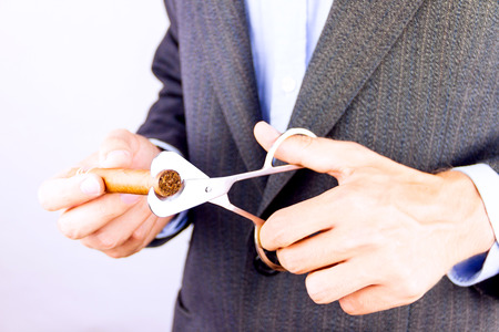 Elegant man wearing suit and blue shirt cutting cigar indoorの写真素材