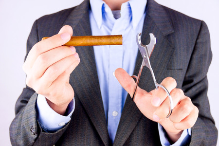Elegant man wearing suit and blue shirt cutting cigar indoorの写真素材