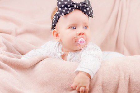 Portrait of a beautiful baby girl with the black band on her head and a binky lying on the sofa