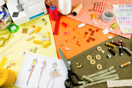 Workplace of a dressmaker: scissors, buttons, spools, measuring tape, sketches, fabric, needles, sewing machine and other tools.の写真素材