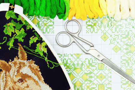 Palette of sewing threads, scissors and hoop isolated on wooden background.