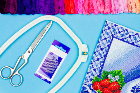 Colorful blue background of sewing items: scissors, needles, embroidery frame, pallet of colorful threads and embroidery pattern. Embroidery and sewing conceptの写真素材