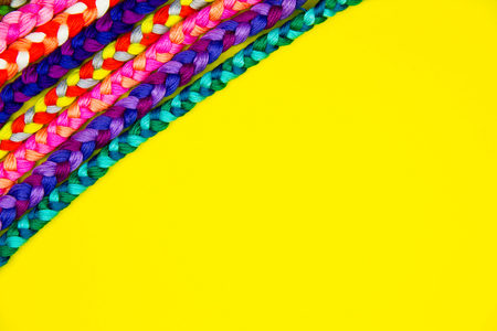 Colorful yellow background of pink, violet, yellow, green, red, purple knitted pigtail. Knitted...