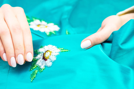 Hands of girl / woman / female sewing colorful flower ornament by beads on blue shirt / dress. Embroidery conceptの写真素材