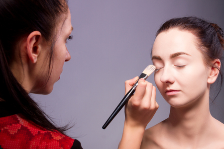 Female / woman / girl preparing for show. Makeup artist with makeup brush for eye doing professional makeup for young woman. Backstageの写真素材