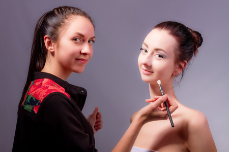 Makeup artist with makeup brush and fashion model smiling while doing makeup. Backstageの写真素材