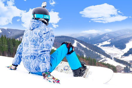 BUKOVEL, UKRAINE - MARCH 12, 2017 Man sitting on the top of the alps mountain  wearing a snowboardのeditorial素材