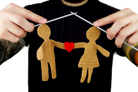 Strict man with tattoo and beard in black t-shirt holding knitted needles with knitted silhouette of female and male in love with knitted red heart shape on isolated backgroundの写真素材