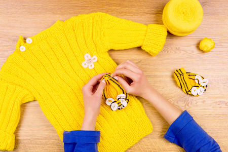 Dressmaker workplace. Woman female hands making yellow baby's bootees and yellow sweater with yellow...