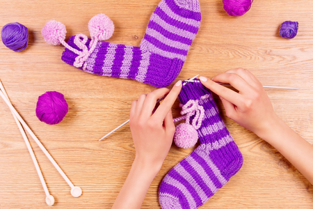 Woman female girl knits a new warm striped violet socks on wooden background. Dressmaker workplace. Top viewの写真素材
