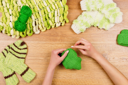 Dressmaker workplace. Female woman hands knitting green socks for kids on wooden backgroundの写真素材