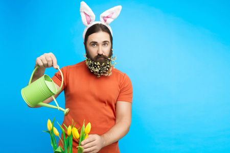 Happy Easter concept. Nice kind muscle man male with watering can watering spring's yellow tulips flowers isolated on blue background. Spring time conceptの写真素材