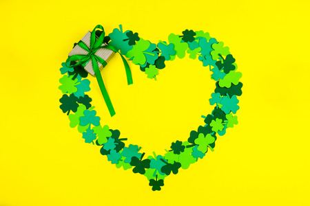 Saint Patrick's Day. Heart shape of green three petal clovers with gift box  lying on yellow backgroundの写真素材
