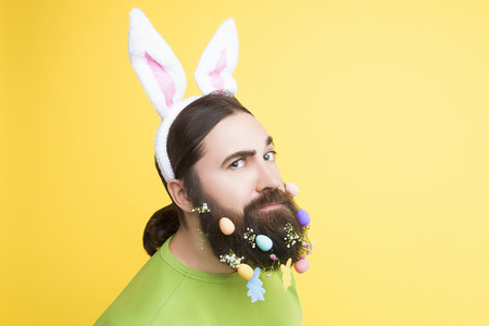 Happy Easter concept. Male man with beard with spring flowers and easter eggs on yellow isolated backgroundの写真素材