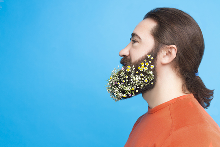 Happy Easter concept. Nice kind muscle man male with beard and spring's flowers in orange t-shirt isolated on blue background. Spring time conceptの写真素材