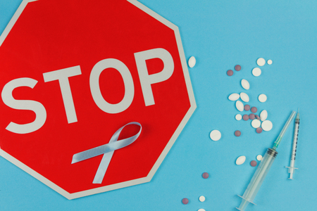 Cyan / Blue tape as symbol of prostate cancer lying with red stop road sign, medicine drugs and  syringe on cyan / blue background の写真素材