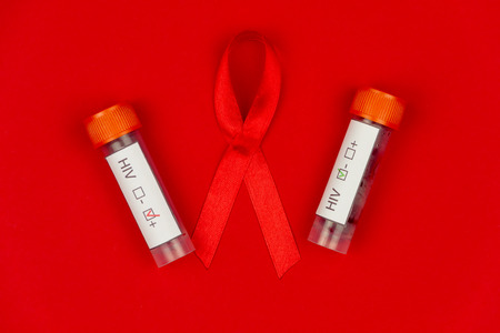 Red tape as symbol of AIDS / HIV illness with blood in test tubes isolated on red backgroundの写真素材