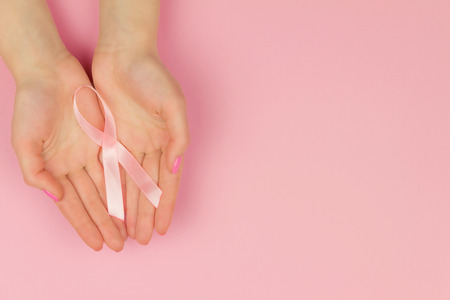Woman hand with pink tape as symbol of women illness mammary cancer isolated on pink background の写真素材