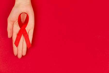 Woman's hands with red tape as symbol of AIDS / HIV illness isolated on red background