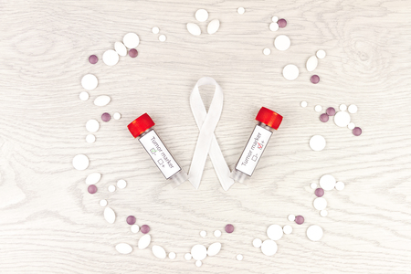 Oncological disease concept. White ribbon as a symbol of lung cancer and tumor markers surrounded by pills  isolated on light wooden backgroundの写真素材