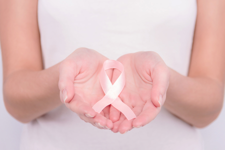 Oncological disease concept. Girl wearing white top holding pink ribbon as a symbol of breast cancer in her hands.の写真素材