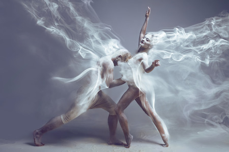 Dancing in flour. Naked couple in love in dust / fog. Girl and guy dancers wearing white sport clothing dancing in flour cloud on isolated background. Surreal concept.の写真素材