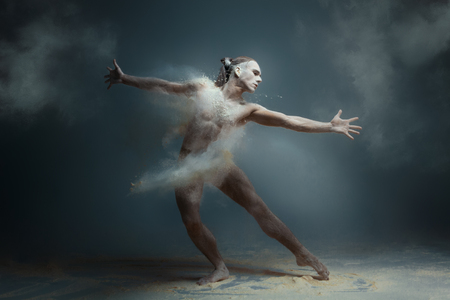 Dancing in flour concept. Long hair muscle fitness guy man male dancer in dust / fog. Guy wearing white shorts making dance element in flour cloud on isolated grey backgroundの写真素材